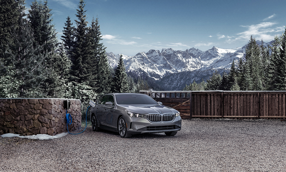 The 2024 BMW i5 eDrive40 plugged into a BMW Wallbox charger in front of a beautiful wintry mountain
    landscape