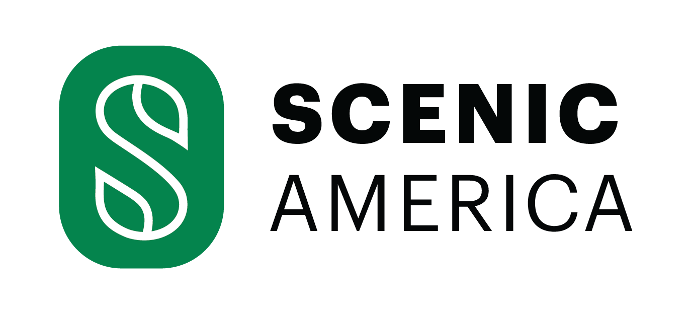 BMW i4, i5, i7 and iX parked in parking lot on side of tree lined road.
