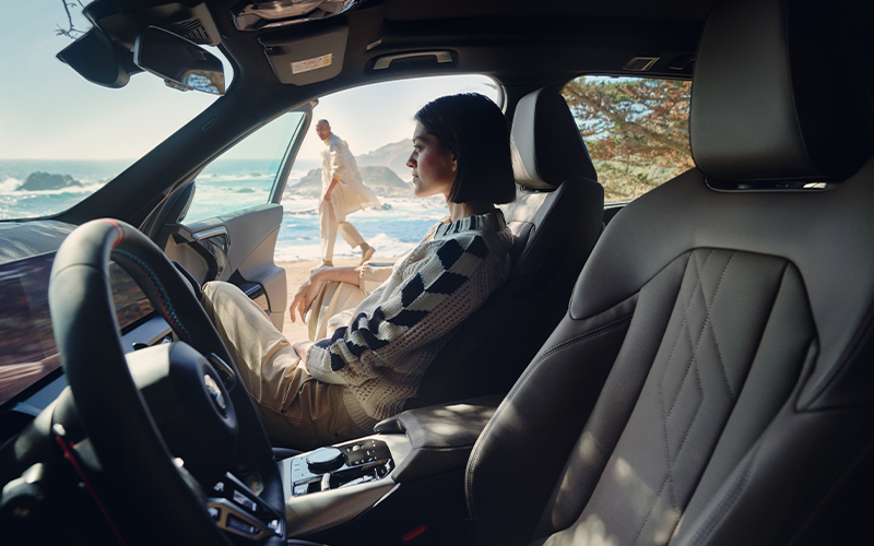 Woman sitting inside of a BMW X3 with a beach background.