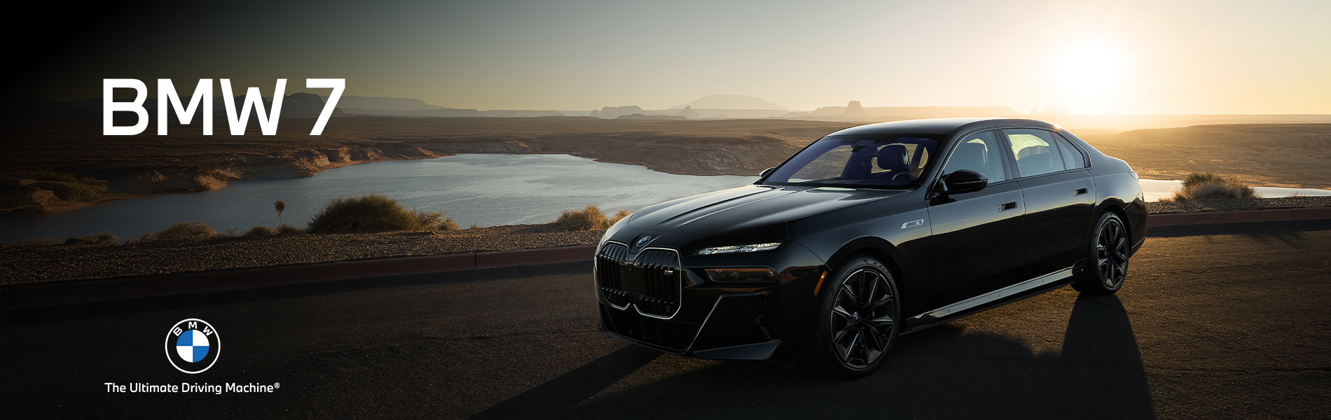 Front and side profile of a black 2026 BMW i7 M70 parked in flat, desert landscape with the sun setting in the background.
