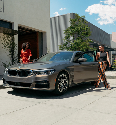 Two women stand next to a BMW parked against a modern building