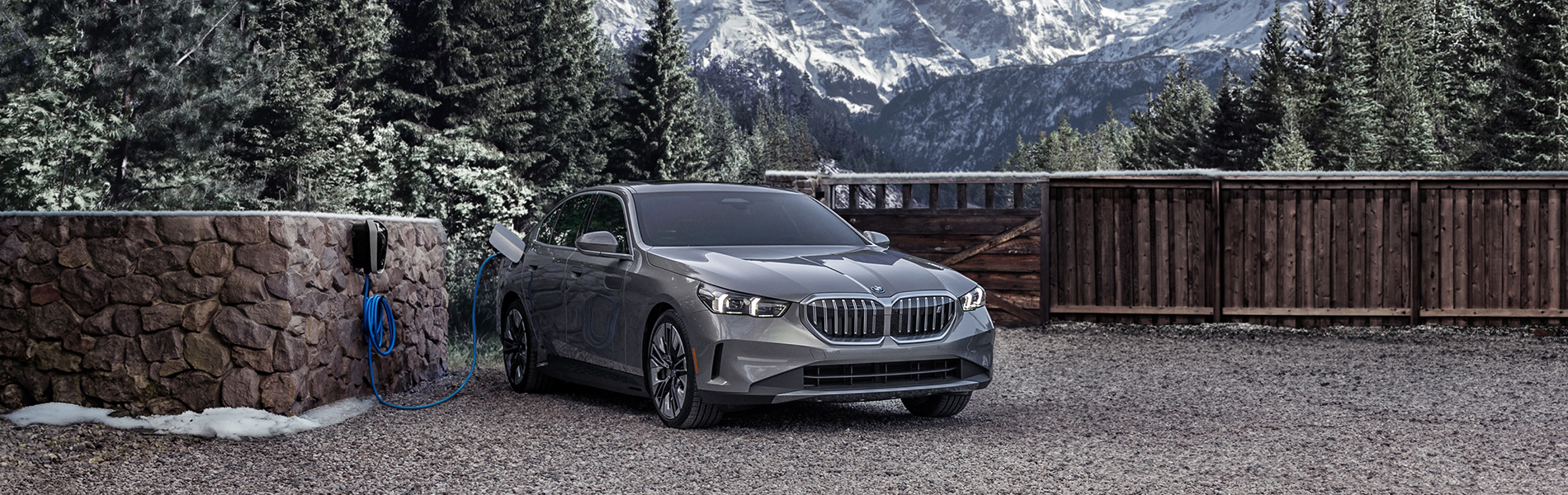The 2024 BMW i5 eDrive40 plugged into a BMW Wallbox charger in front of a beautiful wintry mountain landscape