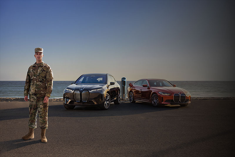 Military man in front of BMW iX and i4 with a
beach setting.