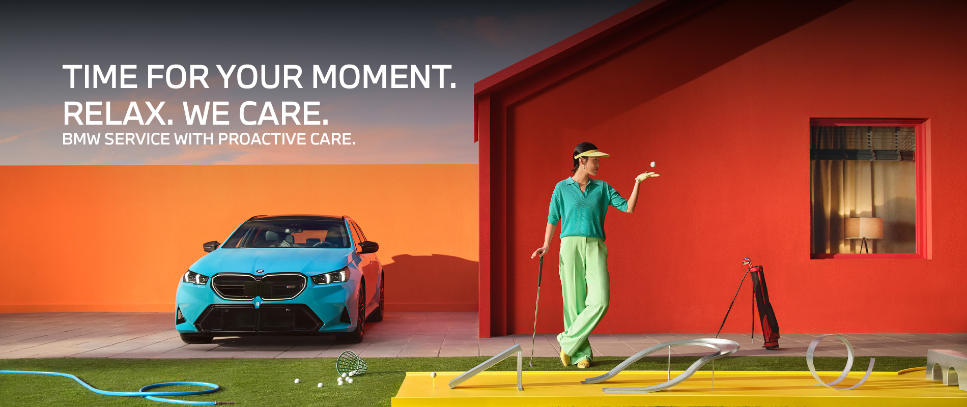 A BMW M5 Touring parked outside a home, with a person holding a golf club near a putting setup on the lawn.