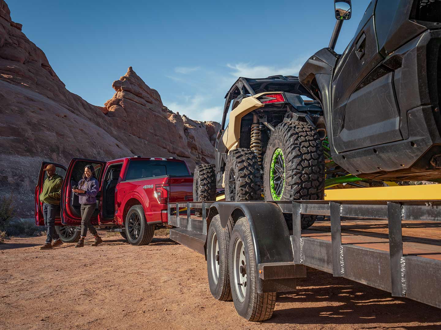 Two people exiting a 2025 Ford F-150® XLT pickup in Rapid Red hitched to a trailer of ATVs