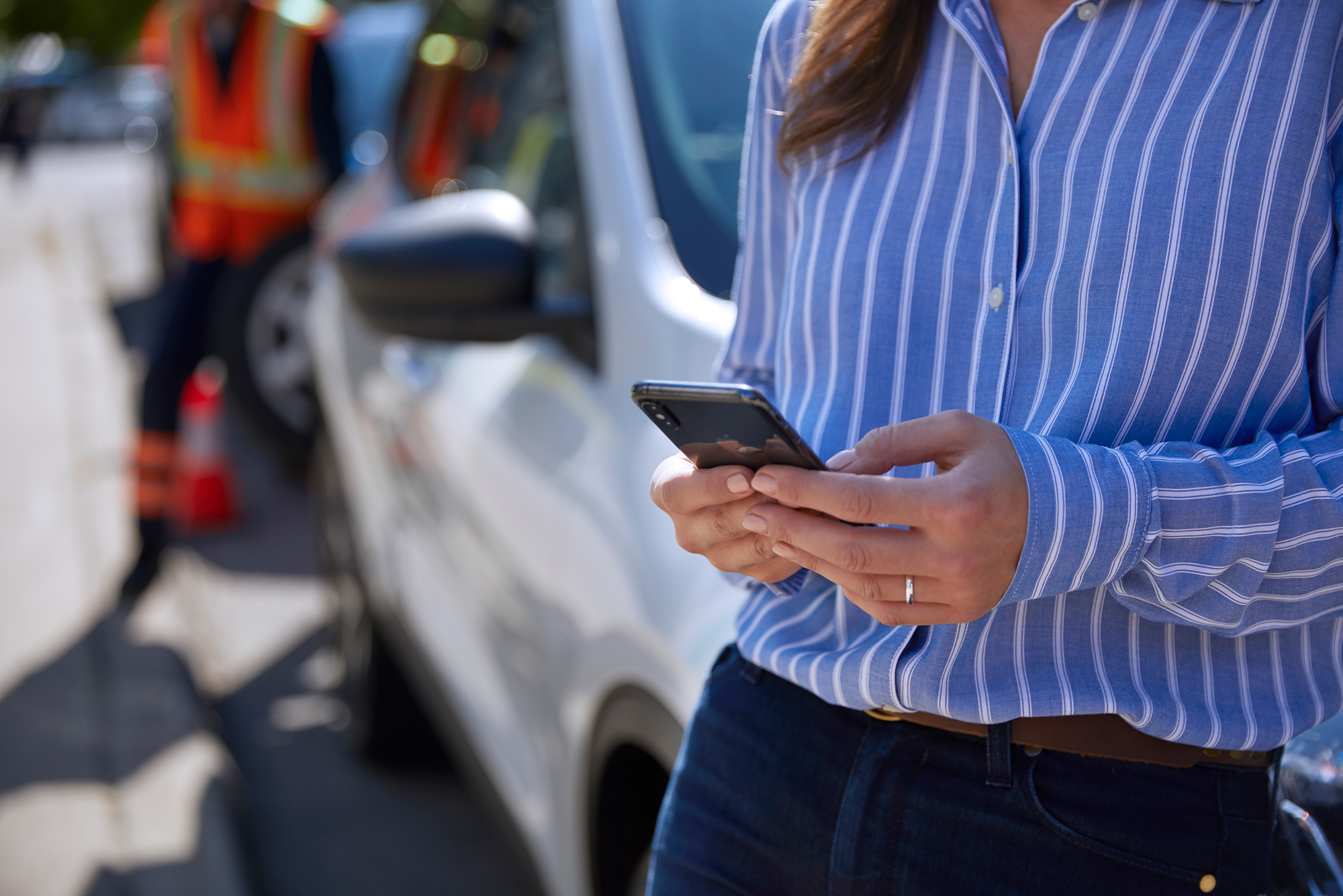 A women using her phone with a Mustang Mach-E in the background