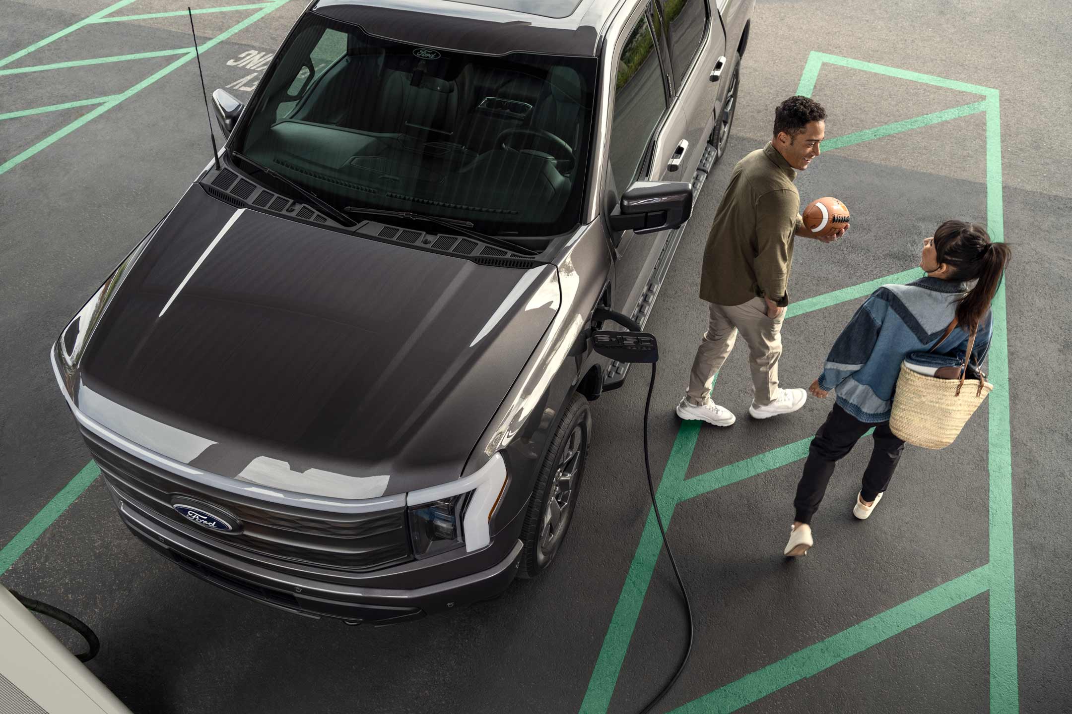 Overhead shot of a couple walking away from a 2024 Ford Lightning® that is plugged in and charging