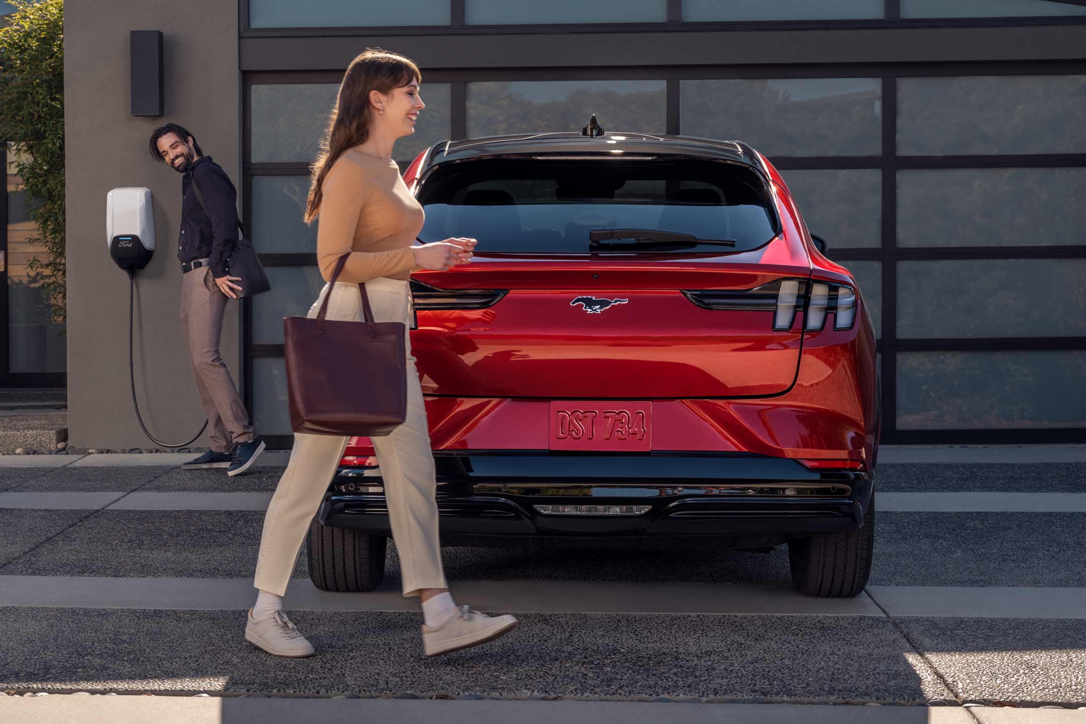 Woman walking in front of a 2024 Mustang® Mach-E charging at home