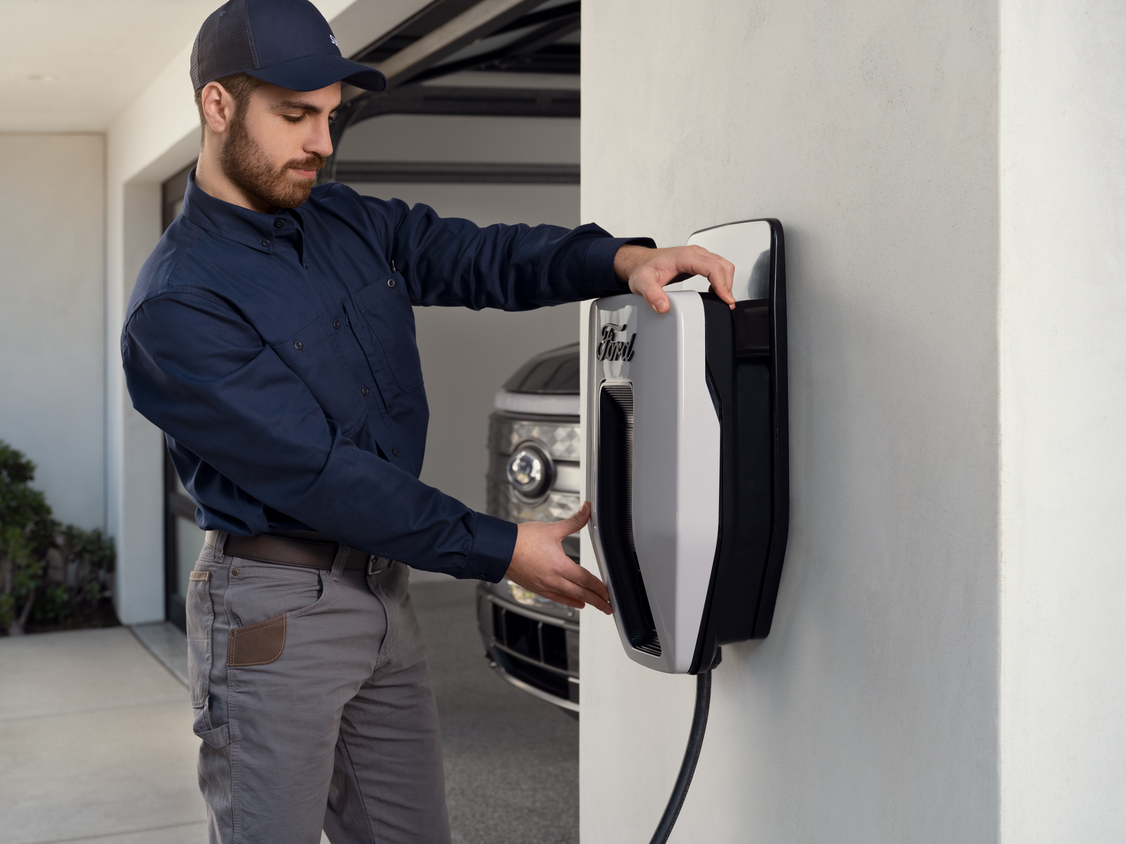 An installer mounting a Ford Charge Station Pro to a wall with a Ford F-150 Lightning® in the garage