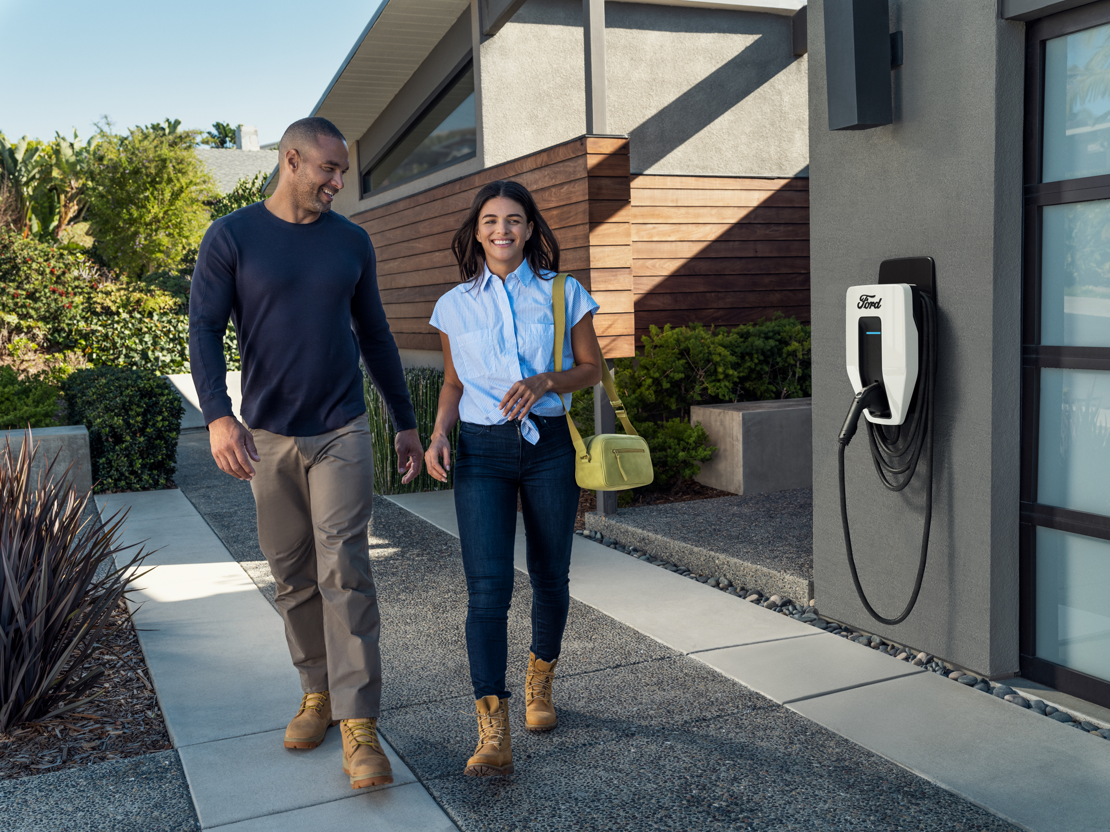 A couple walking out of their home with a Ford Charge Station Pro attached to their garage in the background