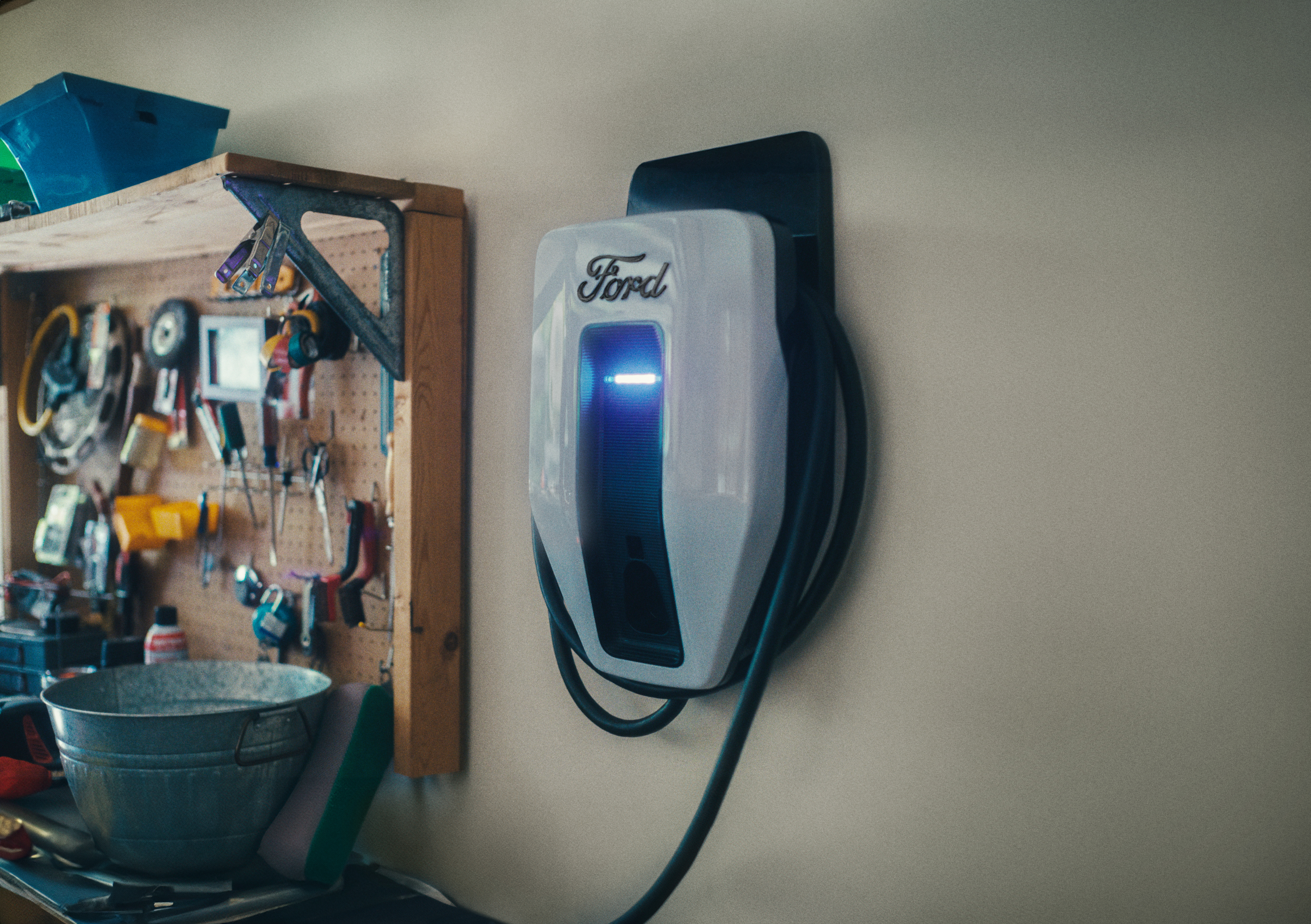 A Ford Charge Station Pro mounted on a garage wall with tools hanging next to it.