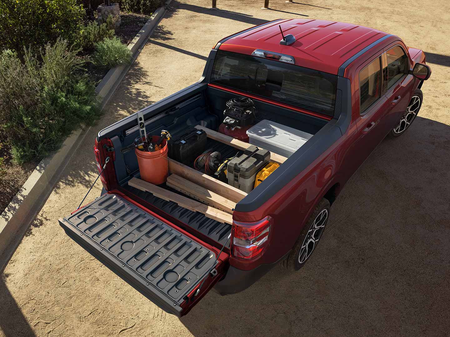 A red Ford Maverick® pickup with gardening items and lumber in the bed, with the tailgate lowered