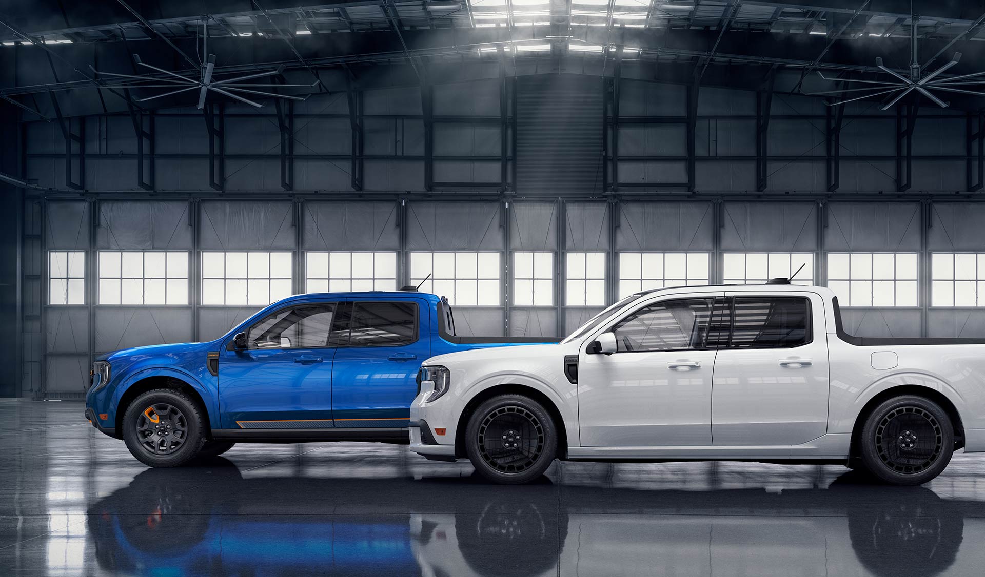 A white Ford Maverick® Lobo™ pickup in front of a blue Ford Maverick® TREMOR® pickup, parked in an aircraft hangar.