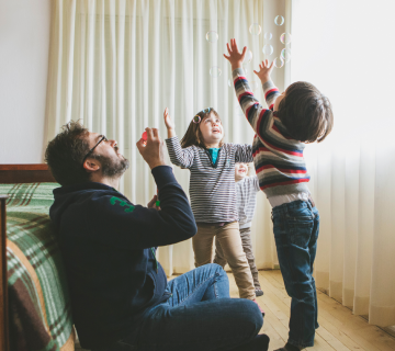 A man and two children catching bubbles indoors.