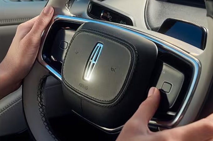 A man holding the steering wheel inside a Lincoln vehicle.