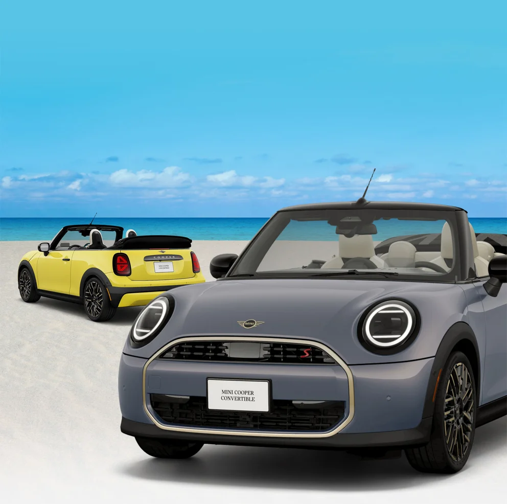 Rear side view of yellow MINI Cooper Convertible behind a front side view of gray MINI Cooper Convertible parked on the
        beach.