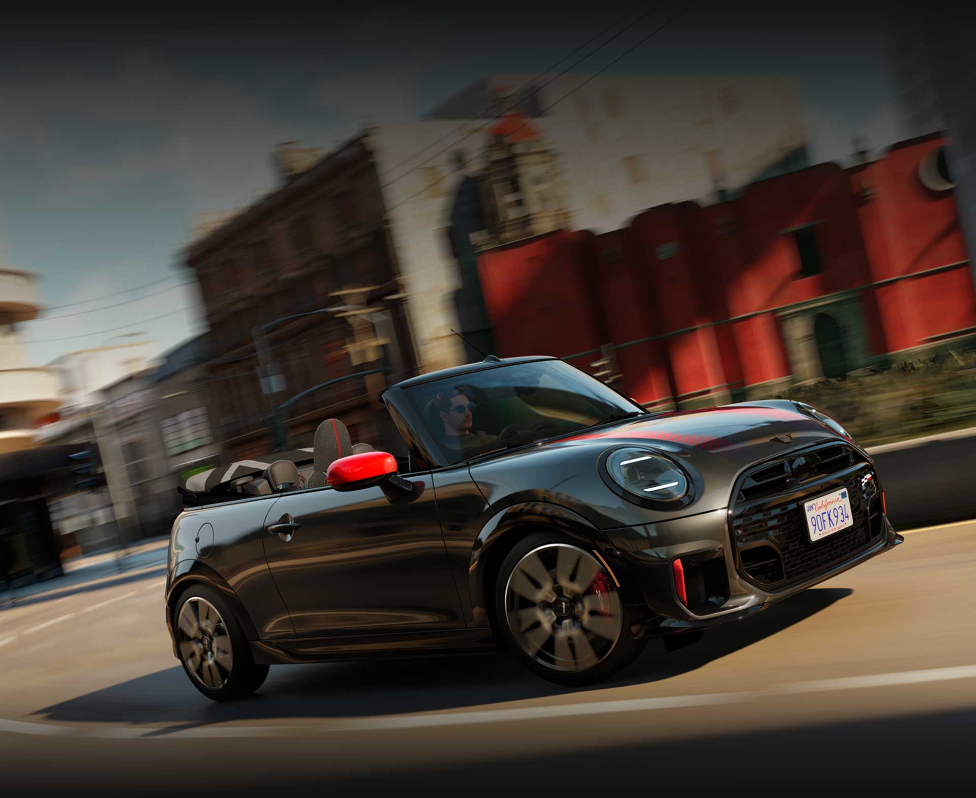 Angled view of John Cooper Works Convertible driving on city street with blurred buildings
        in background.