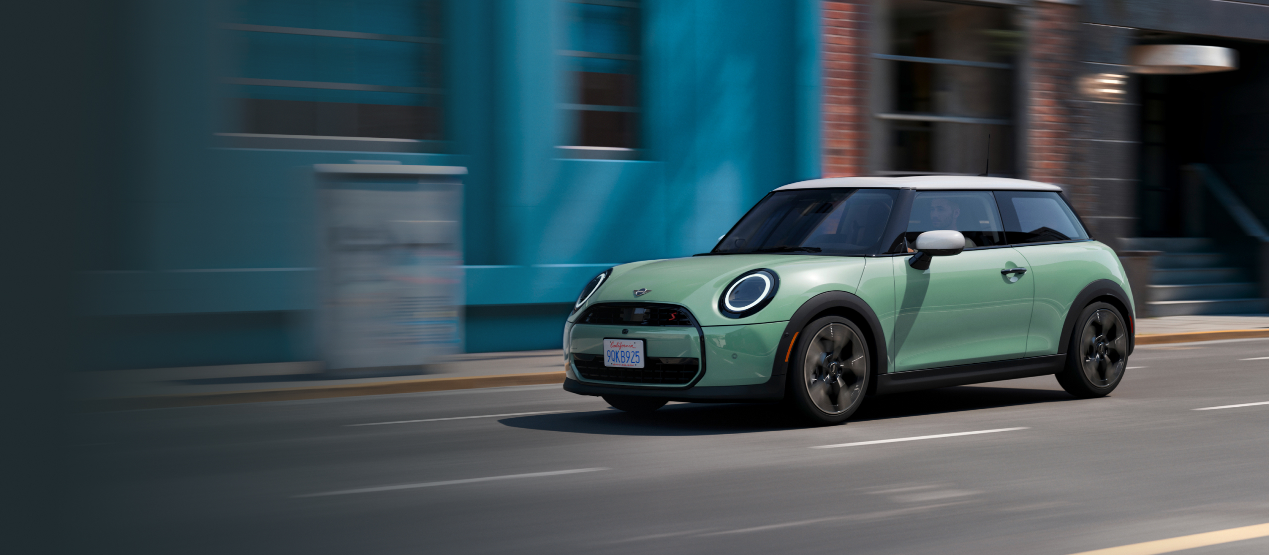  A MINI Cooper S 2 Door in Ocean Wave Green Metallic cruises down a road.