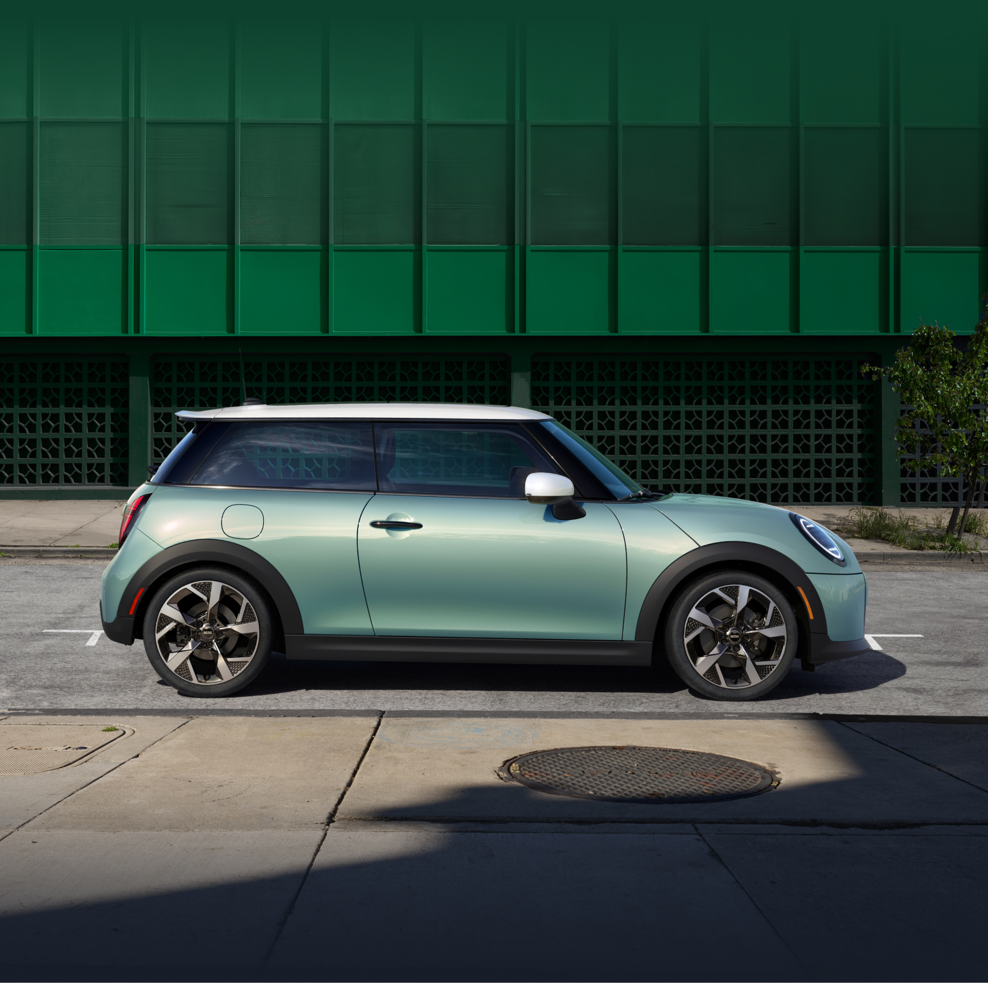 Side-view of a MINI Cooper S 2 Door in Ocean Wave Green Metallic parallel parked against a green wall.