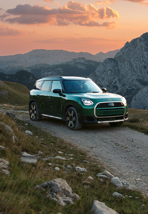 MINI Countryman driving down mountain side with sunset in the background.