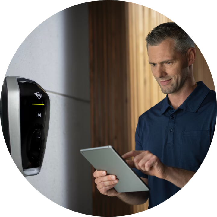 A man looks down at an iPad while standing in front of a home charging device.