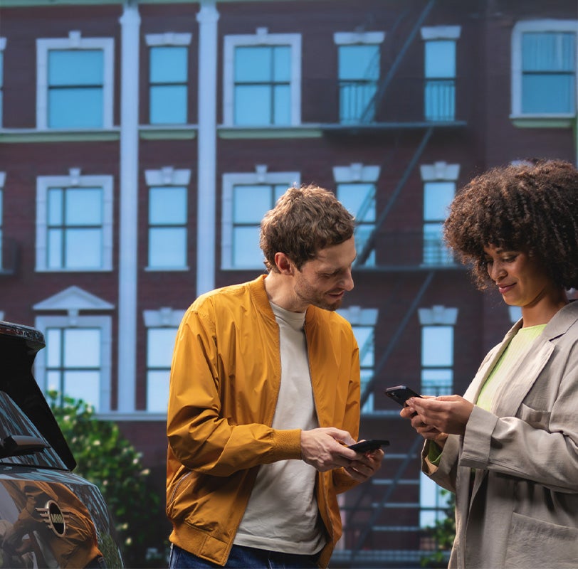 Man and woman looking at phone next to parked MINI