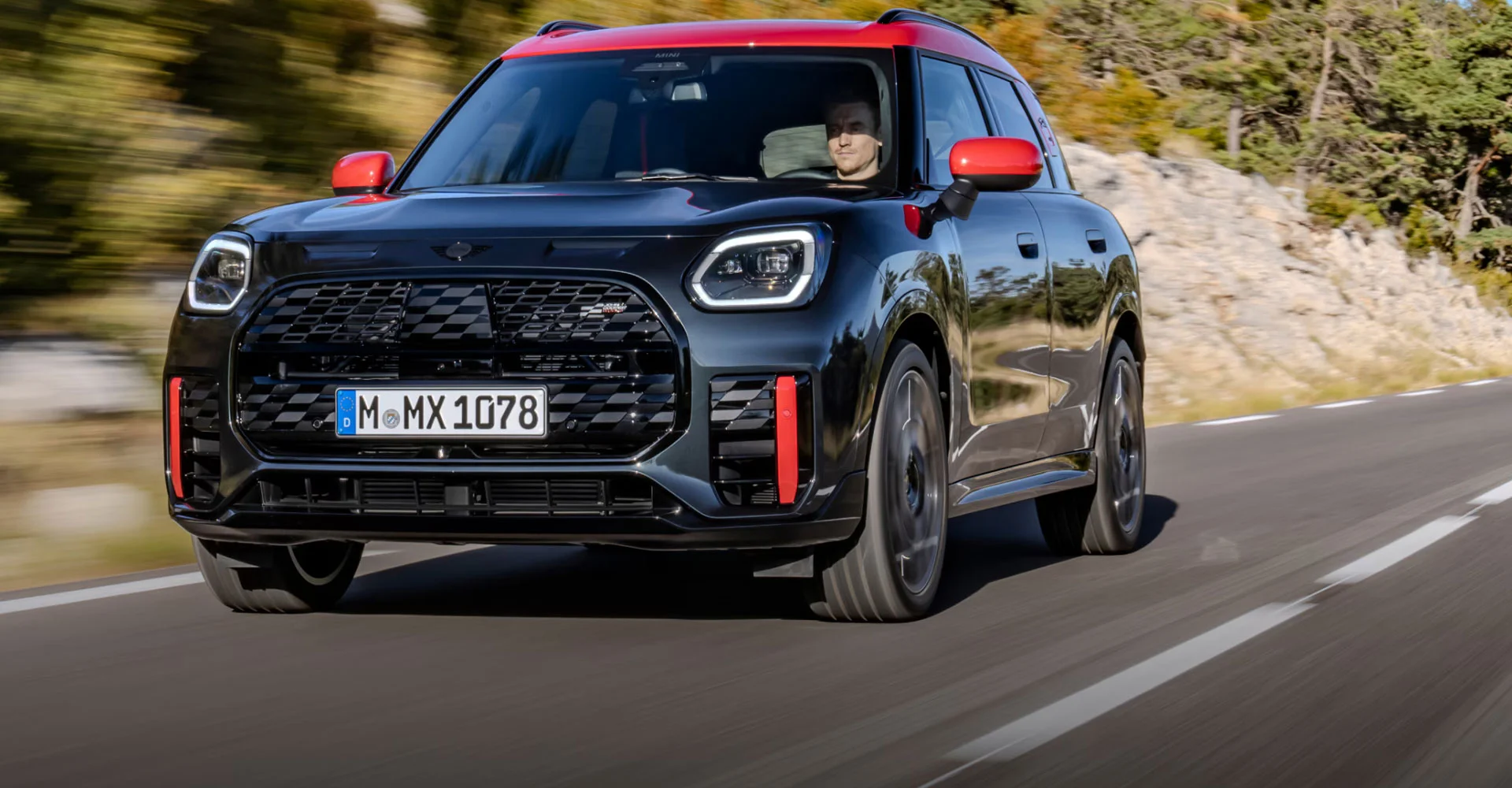 Front view of a MINI JCW Countryman ALL4 driving on a road with a blurred background.