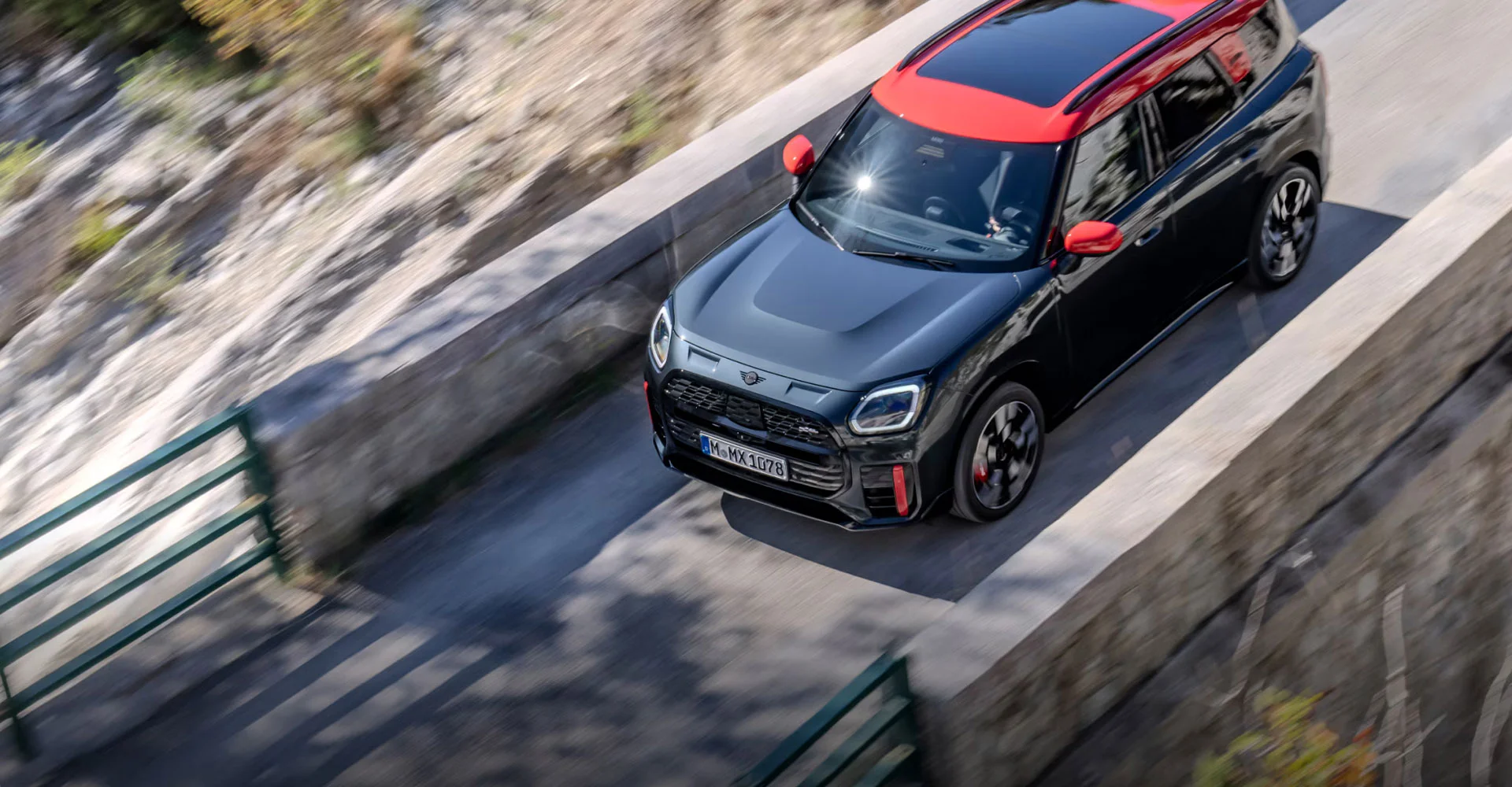 Birds-eye view of the MINI JCW Countryman ALL4 driving over a cement bridge with rock beneath it.