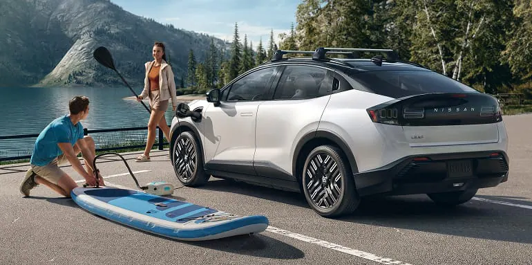 2026 Nissan LEAF 3/4 front view of a Leaf parked lakeside  showing using the vehicles 12-volt AC adapter to charge personal items and cargo
