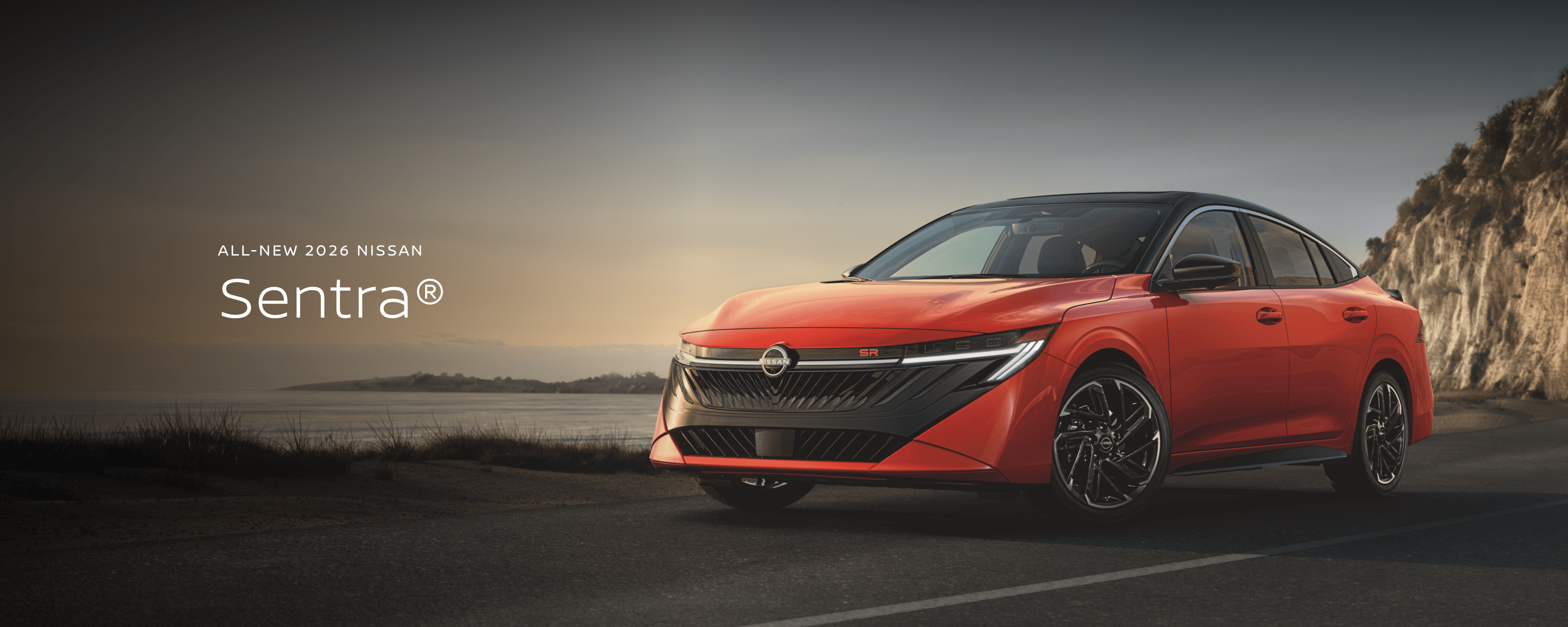 2026 Nissan Sentra in red driving on a desert road with mountains in the distance