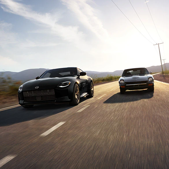 2026 Nissan Z in black driving next to a 240Z on a rural road at speed