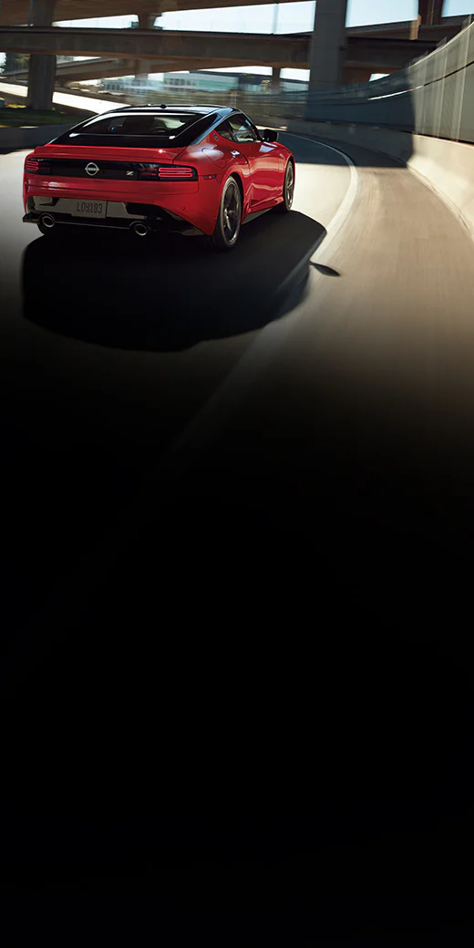 2026 Nissan Z rear view driving down a curved highway beneath a complex set of overpasses