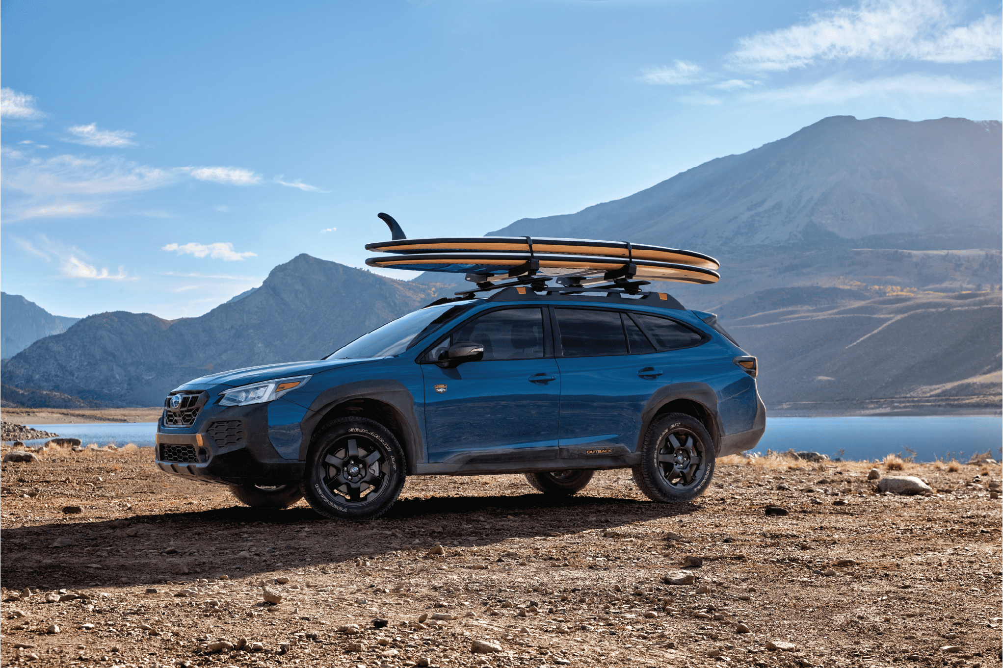 A blue Subaru Outback Wilderness with two surfboards on its roof rack.