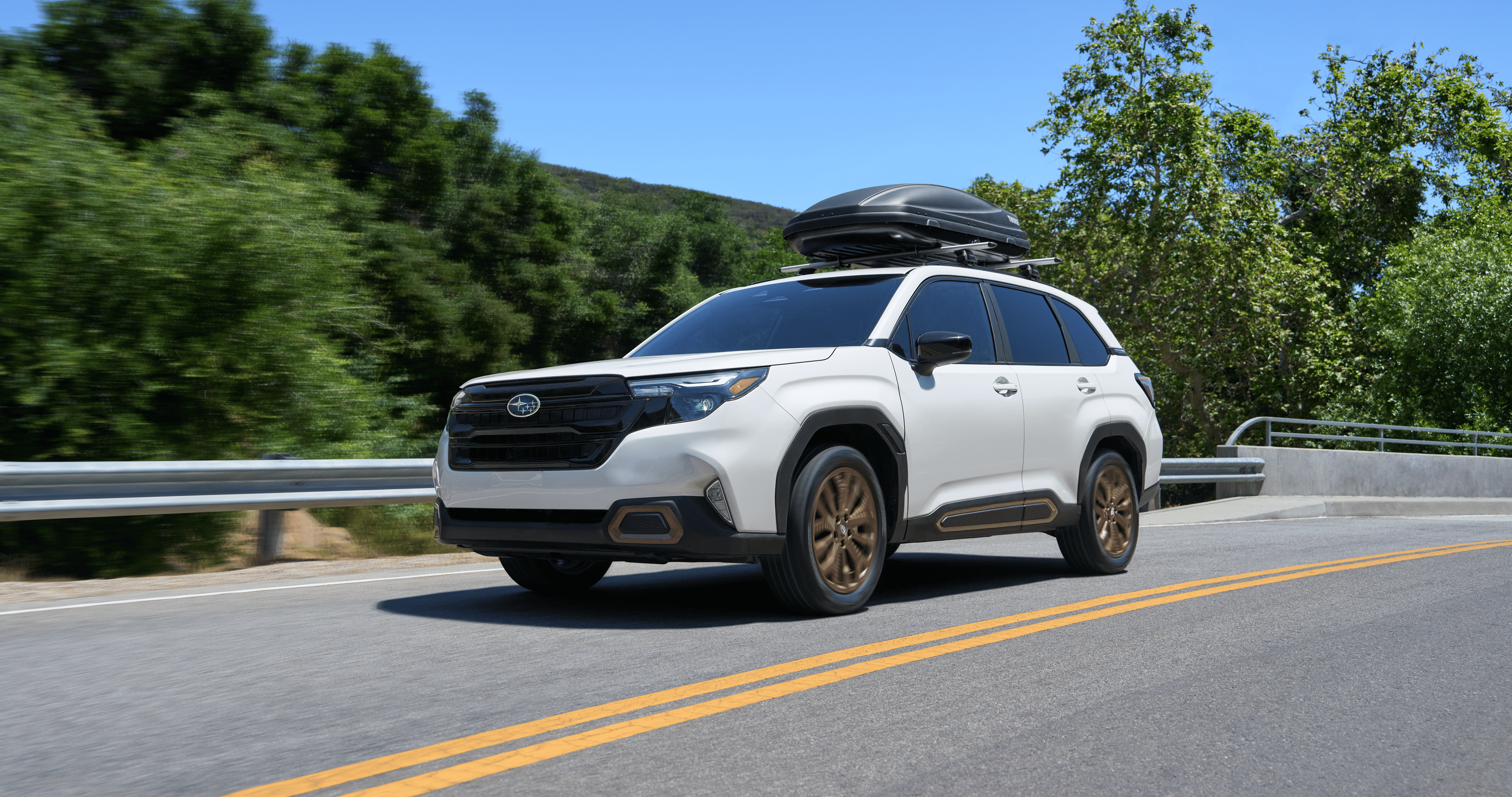  A 2026 Subaru Forester AWD SUV with a Thule storage attachment on its roof rails driving on a highway.