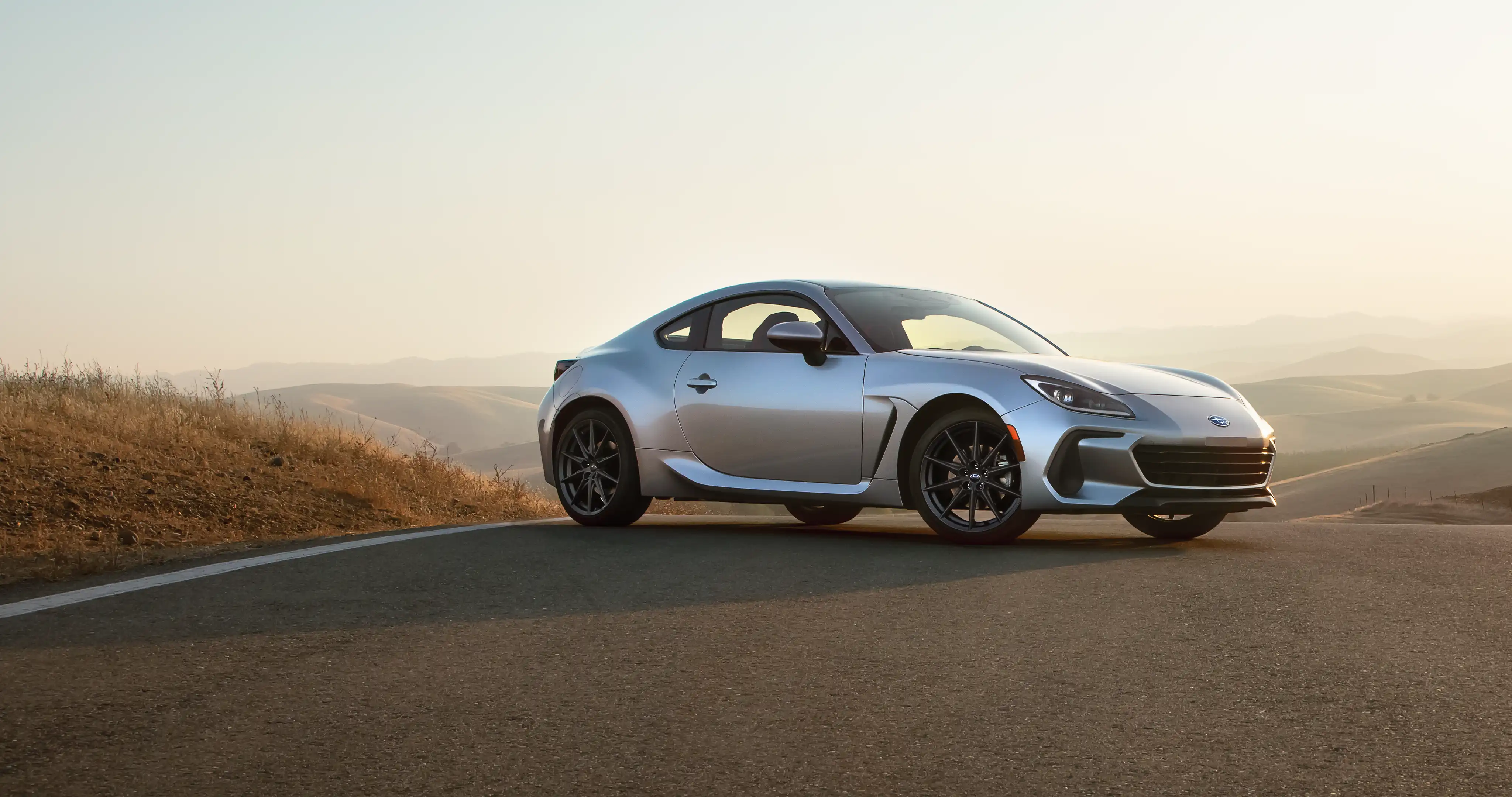  A silver BRZ parked on a road overlooking a hilly landscape.