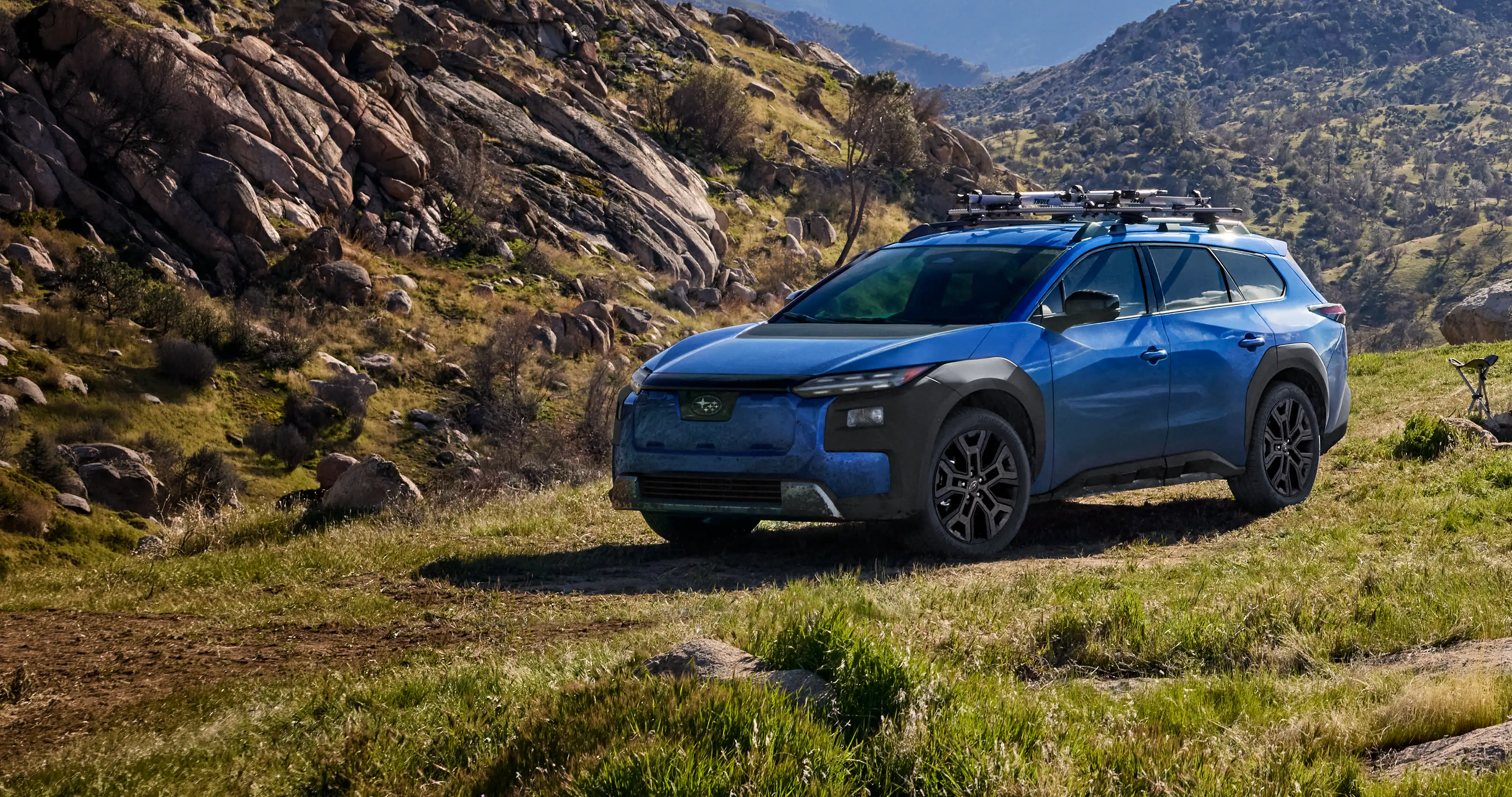 A 2027 Subaru Trailseeker in blue drives down an arid hill.