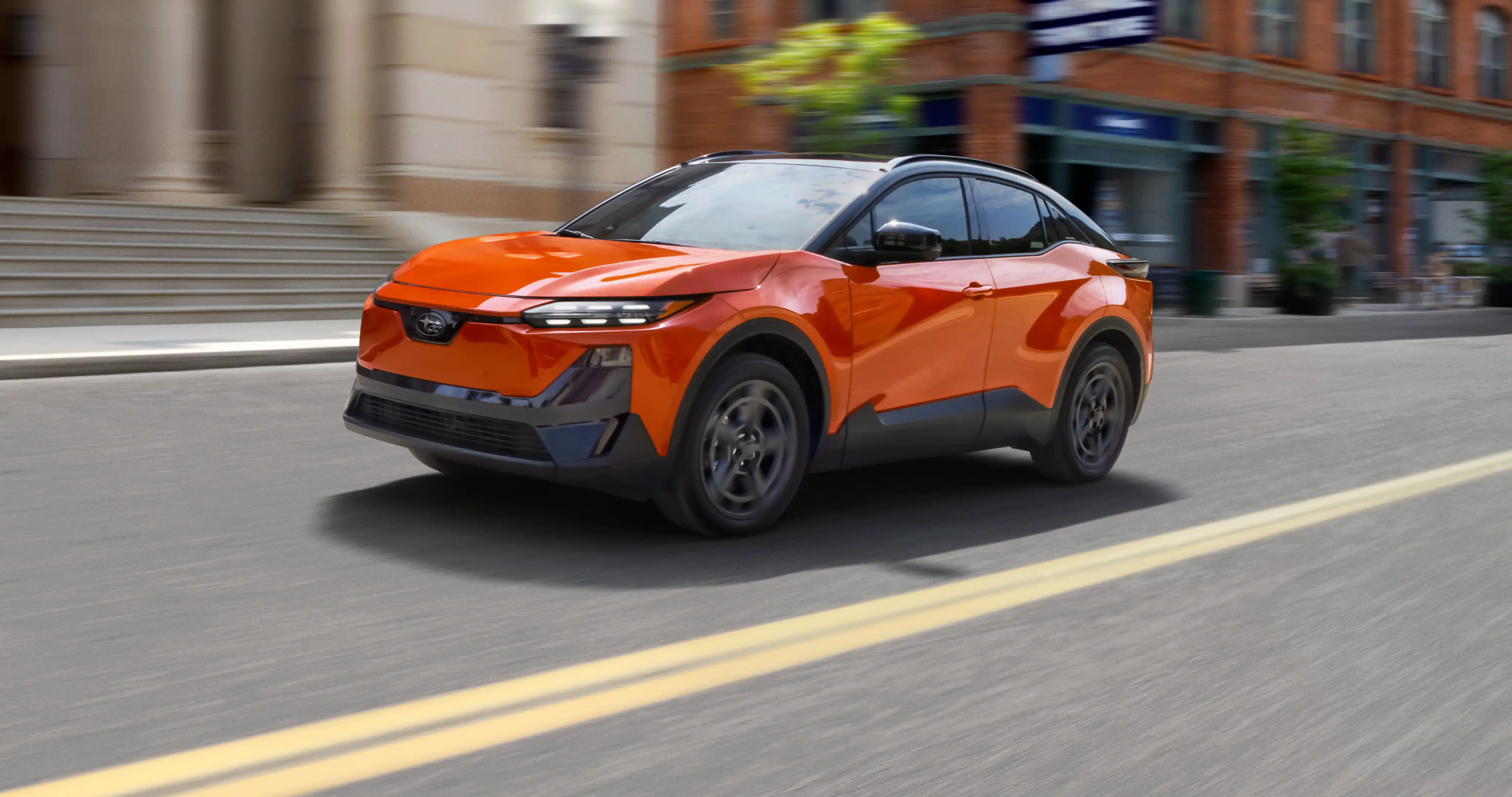 An orange Subaru Uncharted EV drives down a city street.