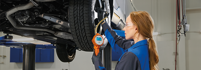 A Subaru technician using flashlight to look into a Subaru engine compartment.