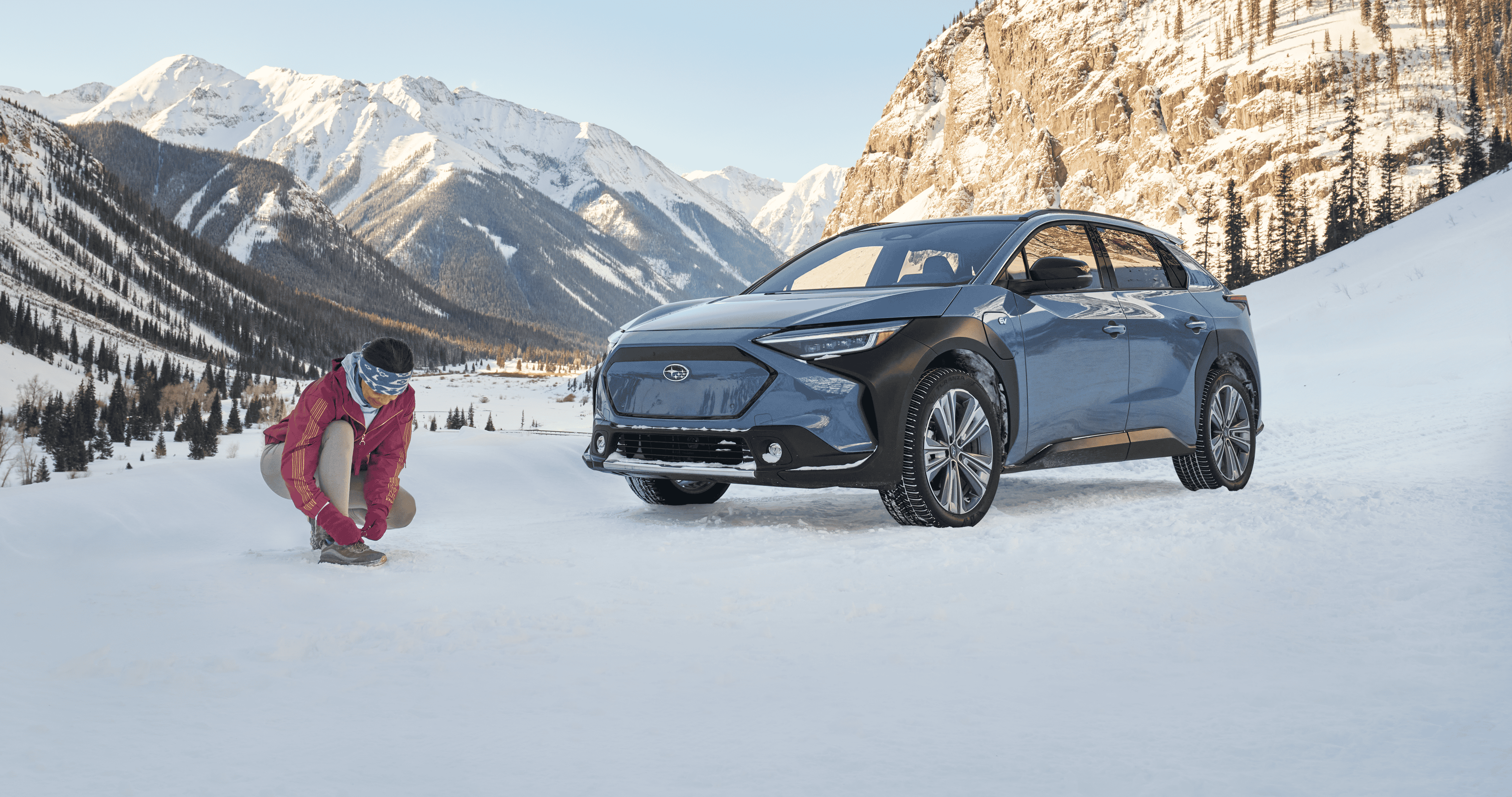 A static image of a blue 2026 Subaru Solterra parked on a snowy mountain landscape.
