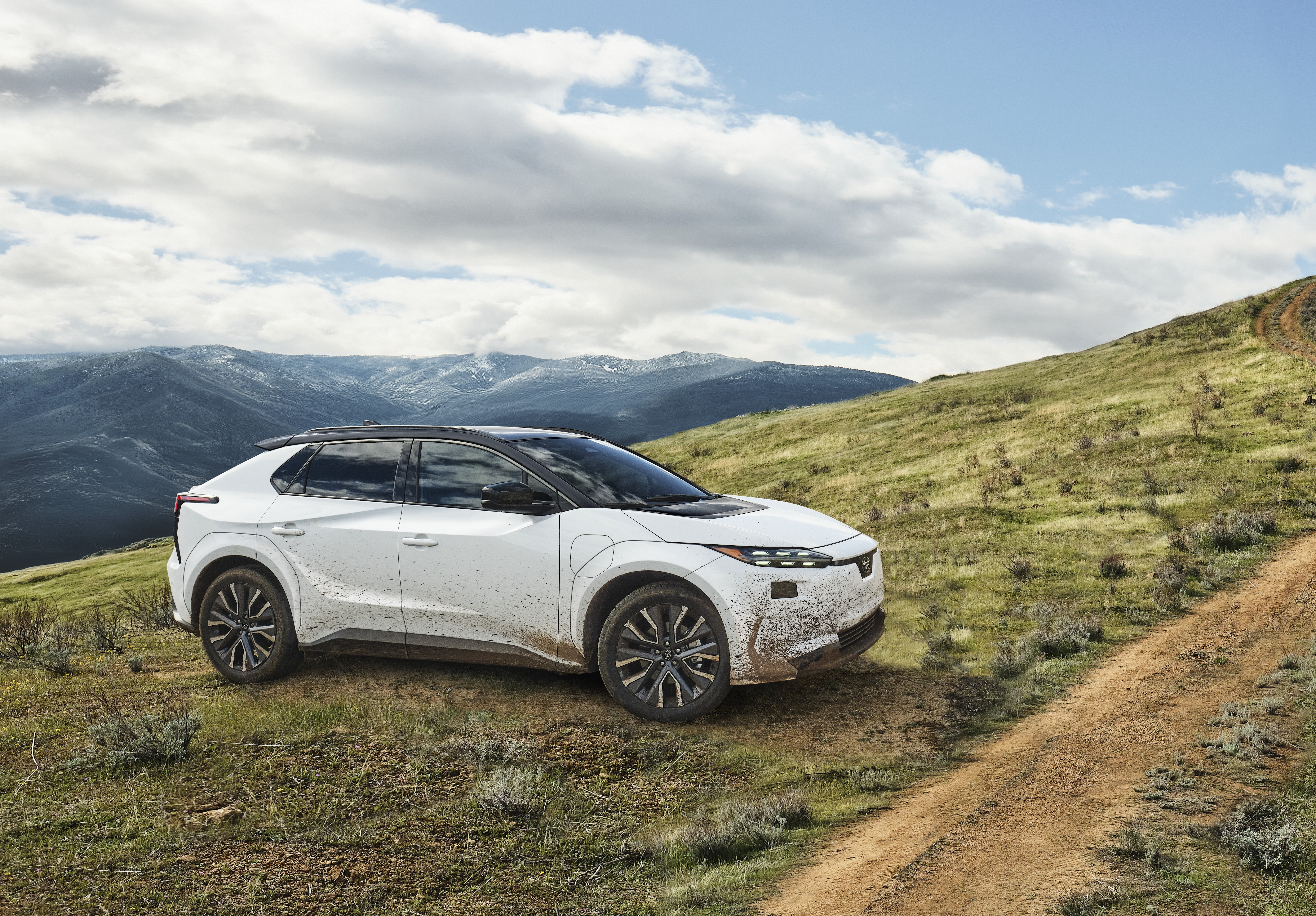 A static image of a white 2027 Subaru Solterra parked on a grassy hill.  

