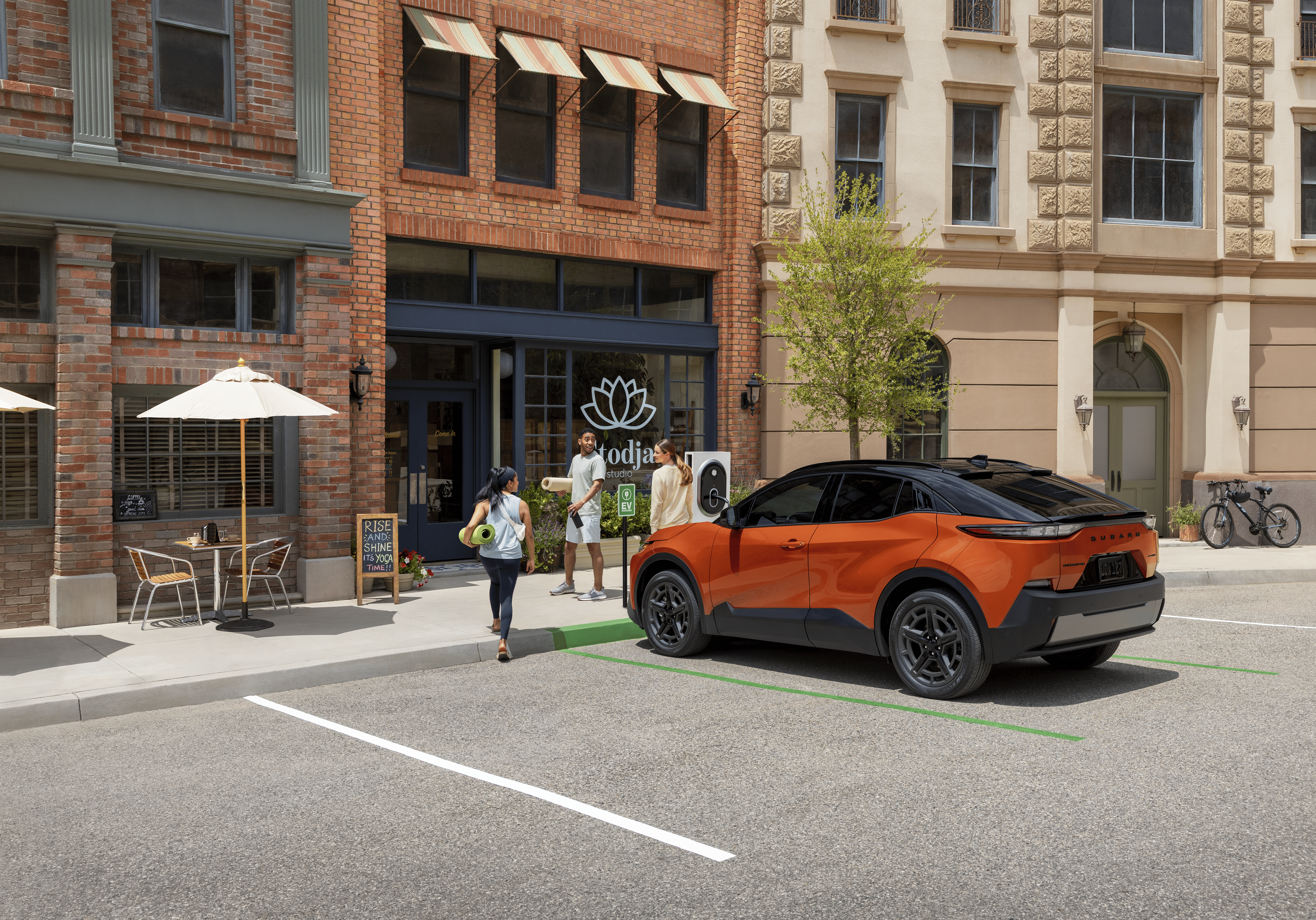 A static image of an orange 2026 Subaru Uncharted parked at an EV charging station along a city street.