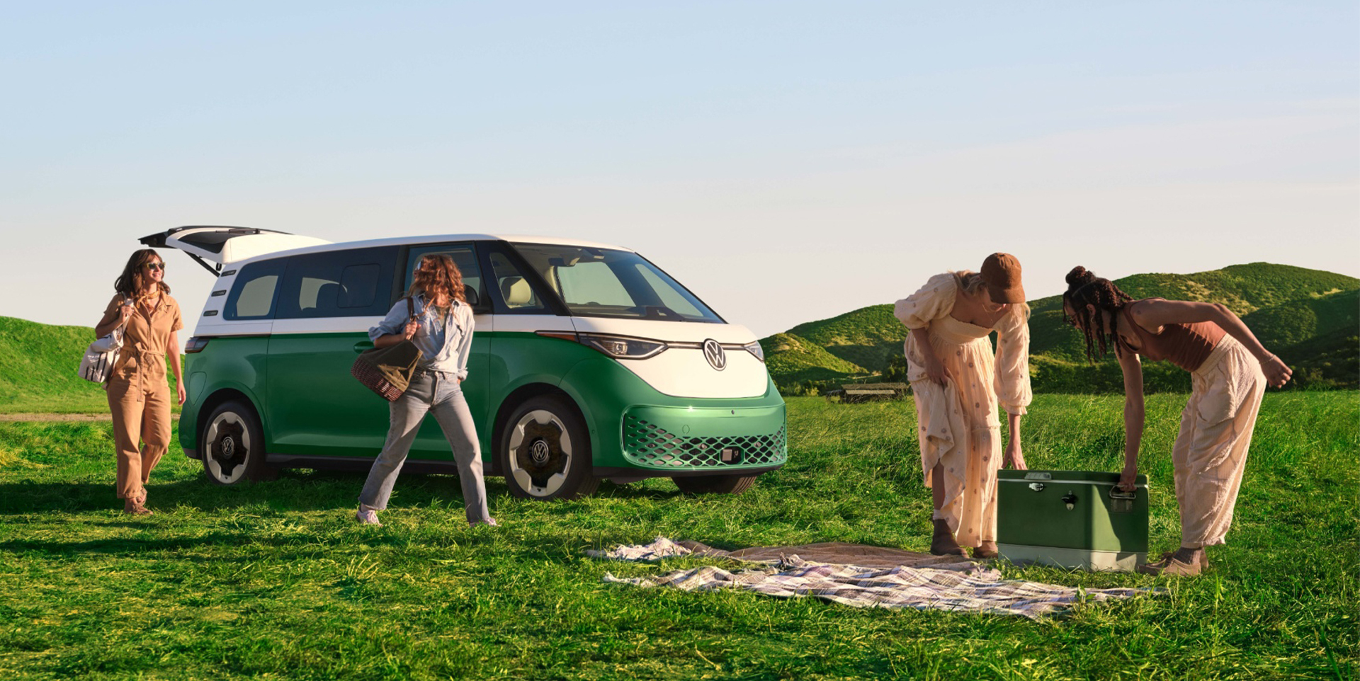 An ID. Buzz shown in Mahi Green Metallic in a grassy field with people outside the vehicle preparing to enjoy the outdoors. 
            