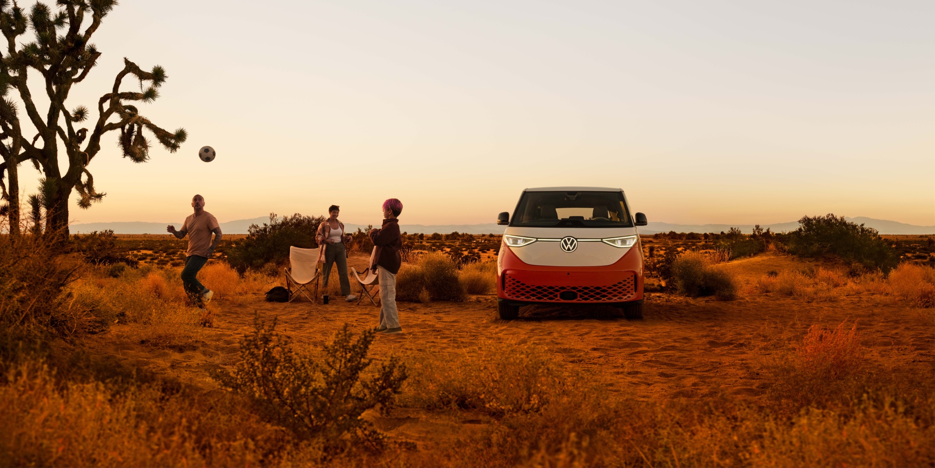 An ID. Buzz shown in Energetic Orange Metallic in a desert landscape with people outside the vehicle preparing to enjoy the outdoors. 