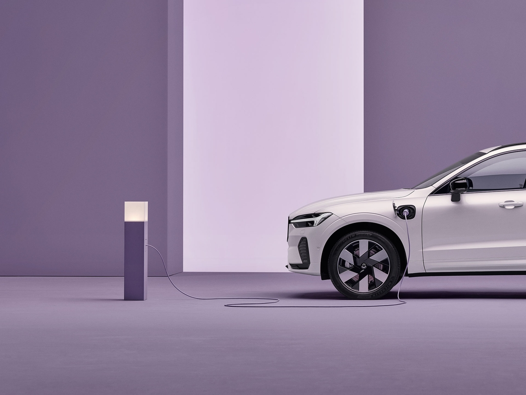 The front half side profile of a Volvo X60 plug-in hybrid car, plugged in to a charging point in an empty, indoor setting.