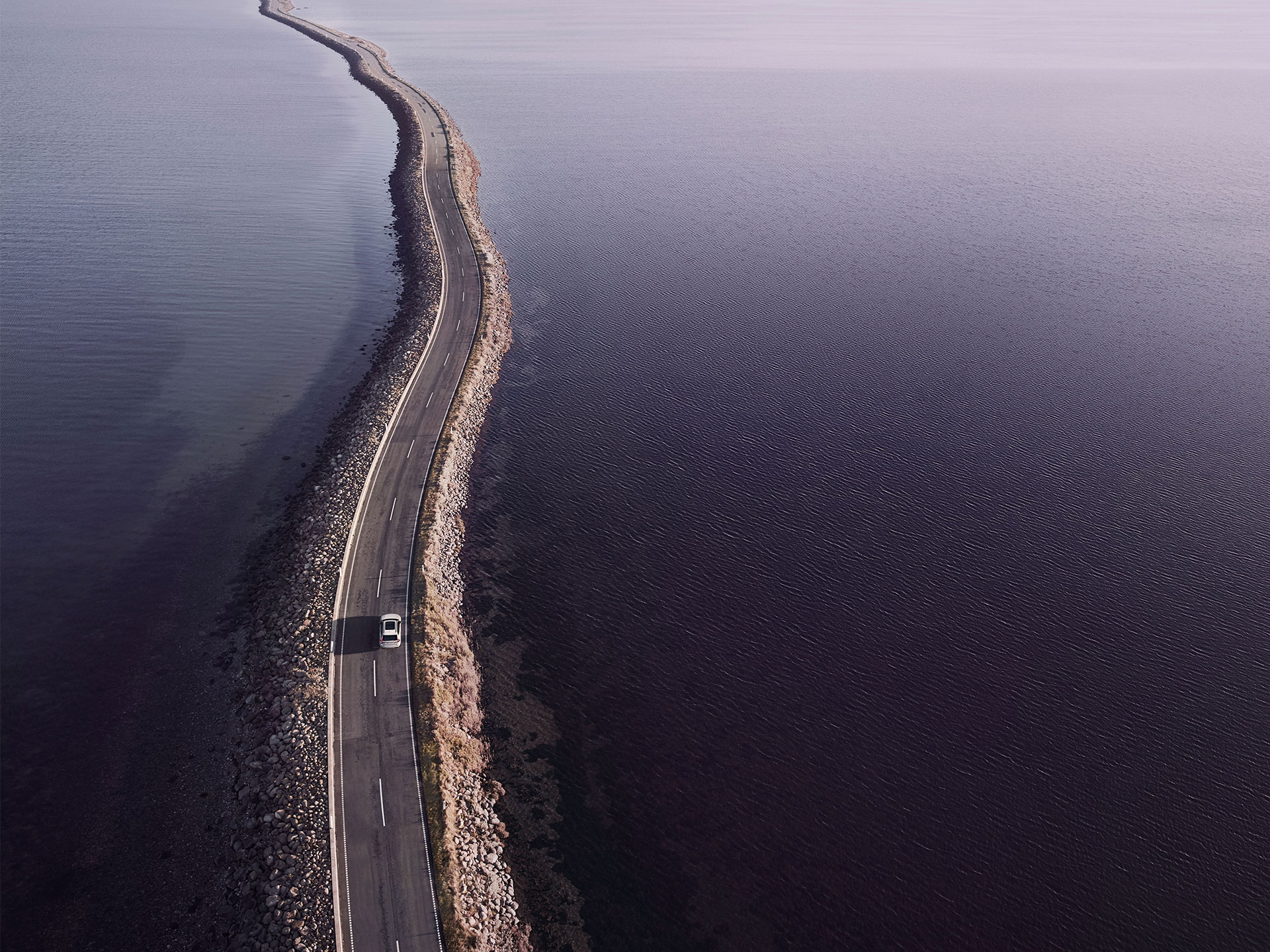A high-angle shot of a Volvo plug-in hybrid SUV driving in Power mode across an ocean road.