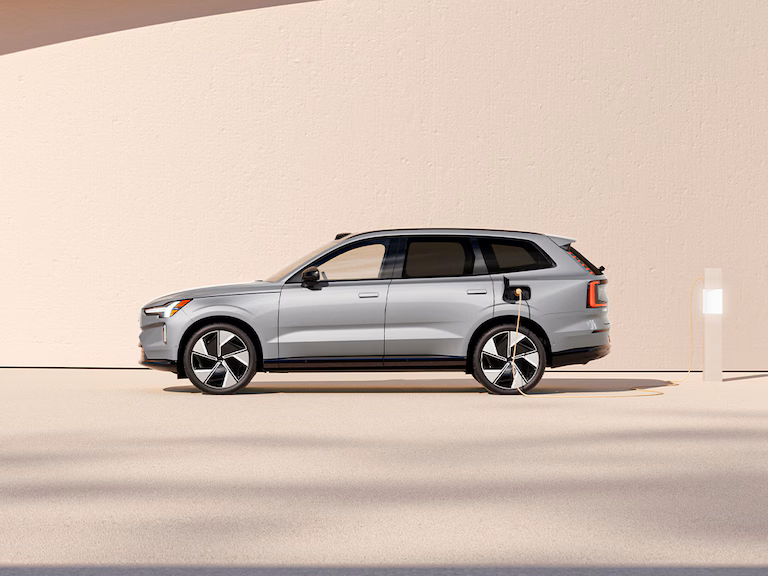 Rear-view of a Volvo EX90 fully electric car on the beach with a man, a dog, and two children running to the ocean.
