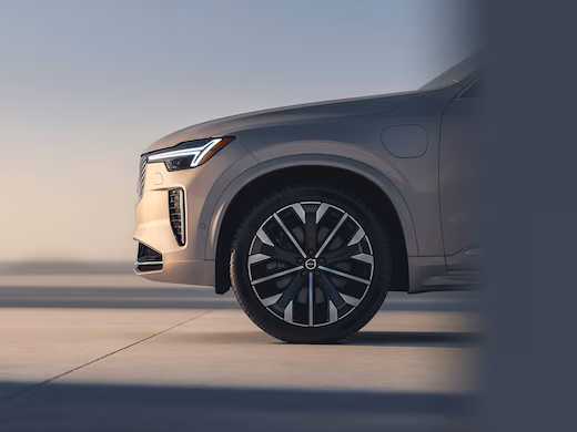 The front half side profile of a Volvo X60 plug-in hybrid car, plugged in to a charging point in an empty, indoor setting.
